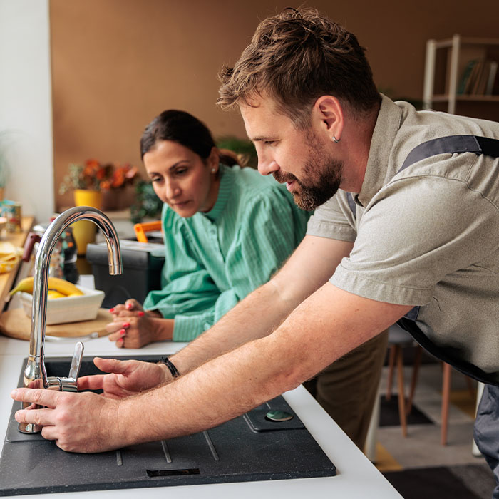 Handyman in work overalls adjusts and inspects the kitchen faucet